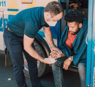 An injured man sitting on the step of an emergency vehicle getting treated by a healthcare worker
