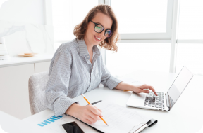 Image of a woman with a notebook, laptop, and calculator in front of her while doing payroll