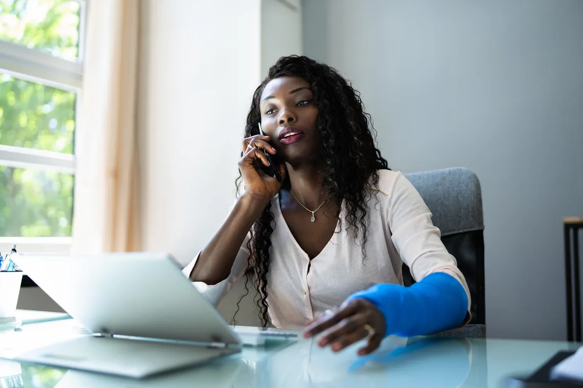 injury woman in blue cast on the phone in front of laptop 1200x800